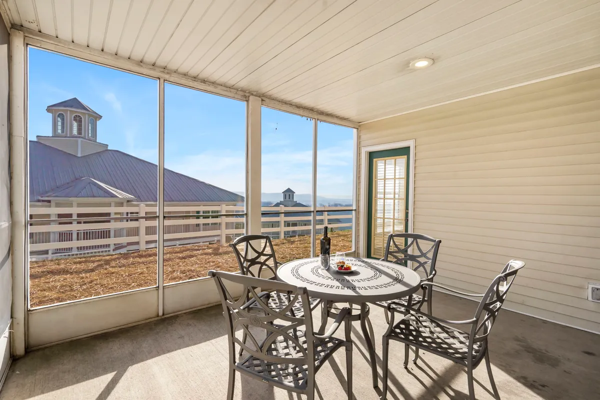 A round table set by generous windows offers views of the outdoors and is arranged with a bottle of wine and a snack platter, surrounded by four chairs. The scene is casual and relaxed, evoking moments of togetherness and enjoyment of sunset or morning light.
