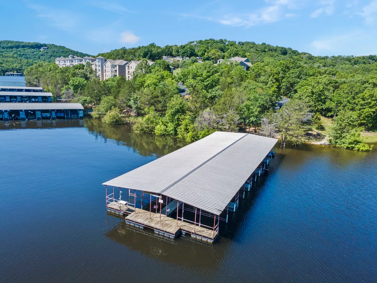 A charming exterior shot of a boat dock nestled among trees, with the water's surface glinting and residential buildings in the background. The setting is intimate, inviting guests to imagine fishing, boating, or strolling along the dock at sunset.
