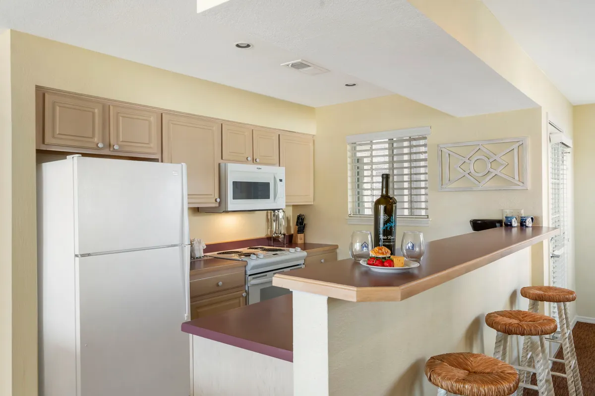 A stylish kitchen island with bar stools, fruit arrangements, and modern appliances. This perspective emphasizes the kitchen’s role as a social hub, where guests can sit and connect as meals are prepared. The space appears open, airy, and welcoming, ideal for both cooking and casual dining.