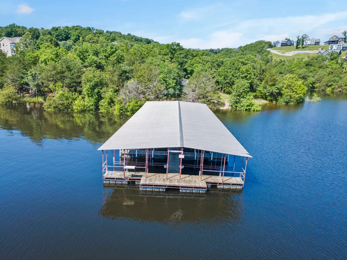 A serene dock extends over the water, framed by lush greenery and a waterfront structure. The tranquil setting evokes moments of relaxation, nature watching, and easy access to the lake for outdoor activities.