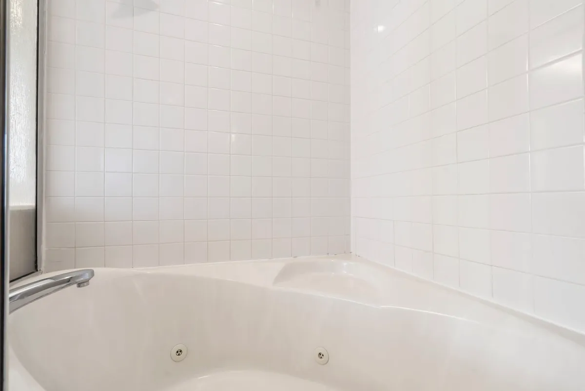A modern bathroom with a luxurious whirlpool tub, white tiled walls, and a showerhead. The serene, spa-like ambiance suggests a perfect place for relaxing baths or rejuvenating self-care routines after a day of adventure.
