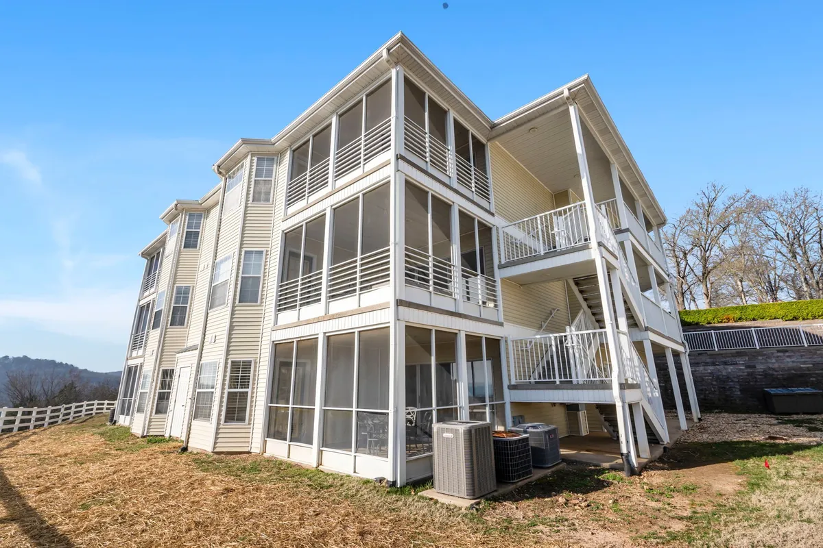 An exterior view of the condo showcasing balconies, screened-in porches, well-kept landscaping, and distant mountain views. The tranquil setting invites outdoor relaxation and group gatherings.