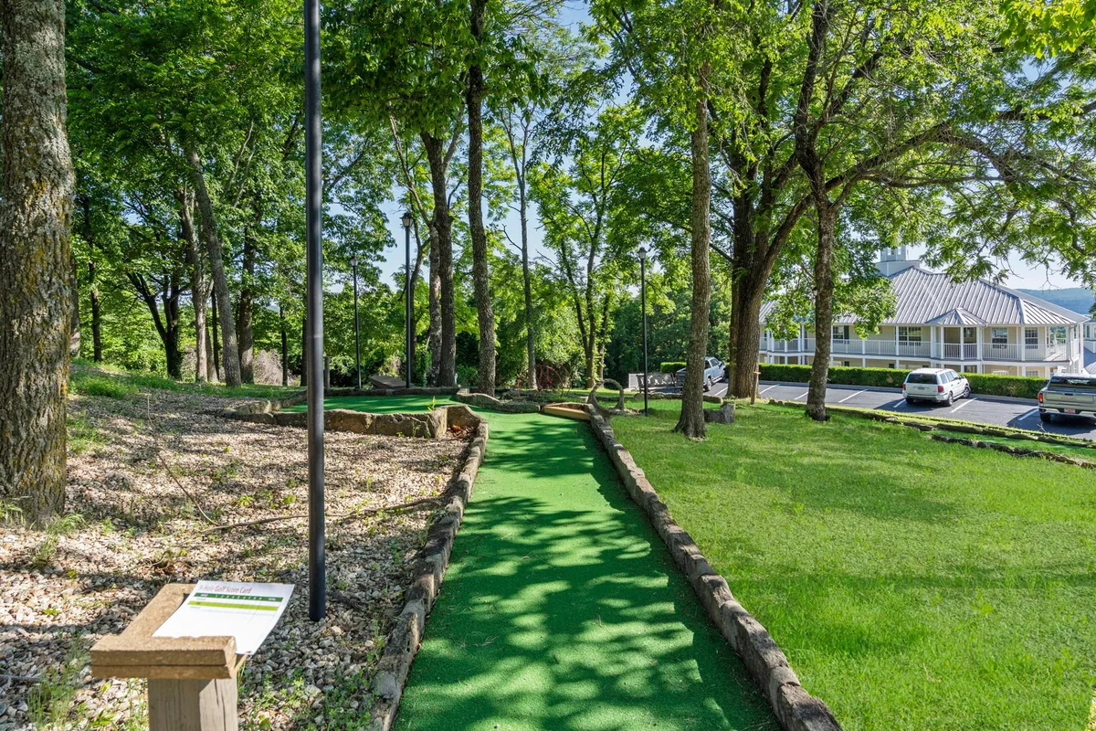 A playful mini-golf course is nestled among lush greenery with a visible sign providing course information. The area looks inviting for families and groups, with clear pathways and sheltered spots for breaks between games.