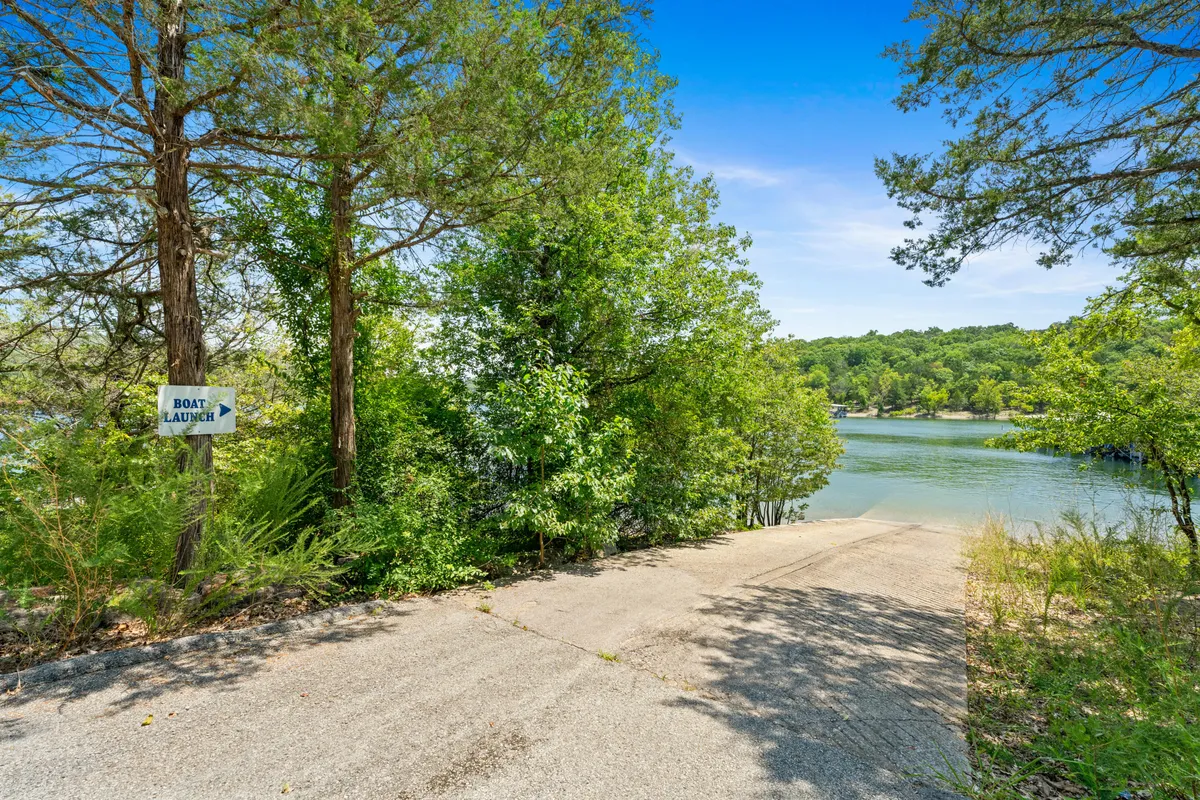 A clear shot of the community boat ramp shows a concrete ramp descending into the lake, surrounded by vibrant greenery and signage. The image also hints at walking trails and picnic-friendly spaces, plus easy access to lake adventures.